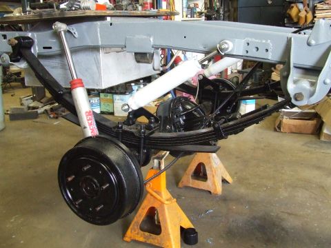 1967 Ford Bronco - Close-up of vehicle suspension and brake assembly, supported by jack stands in a workshop.