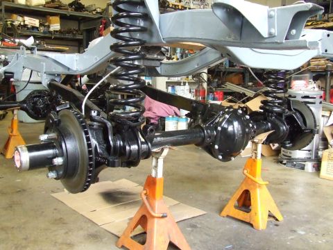 1967 Ford Bronco - The chassis and suspension components of a vehicle are displayed on jack stands in a workshop setting.