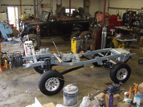 1967 Ford Bronco - The chassis and powertrain components are laid out in a garage, with a vehicle body suspended above.