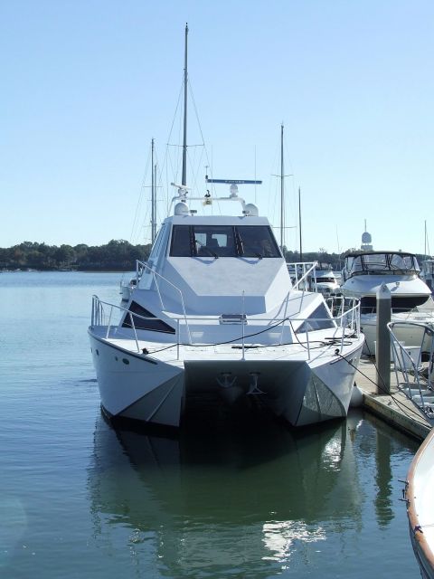 1976 Ford F-150 - A white catamaran yacht is moored in a harbor with other boats visible in the background.