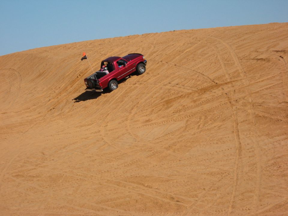 Red Ford Bronco with safety flag climbing a sand dune covered in tire tracks