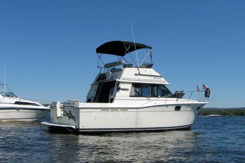 1985 Carver 326 Aft Cabin - A white motor yacht named Drifter is docked on blue water under a clear sky, with another boat visible to the left.
