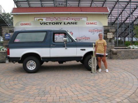 1995 Ford Bronco - A woman stands with a trophy next to a two-tone blue and white 1995 Ford Bronco at Maple Grove Raceway's Victory Lane.