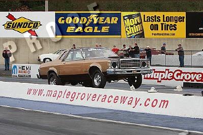 1995 Ford Bronco - A brown sedan, likely a 1977 model, is staged at Maple Grove Raceway with advertising banners in the background.