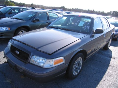 2001 Ford Crown Victoria - A dark gray Ford Crown Victoria is parked in an outdoor lot with its hood up, showing other vehicles nearby.