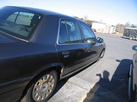 2001 Ford Crown Victoria - This dark sedan, believed to be a 2001 Ford Crown Victoria, is viewed from the side, highlighting its chrome wheel covers and tinted window…