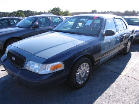 2001 Ford Crown Victoria - A two-tone blue 2001 Ford Crown Victoria is parked in an outdoor lot with other vehicles, displaying visible wear and tear.