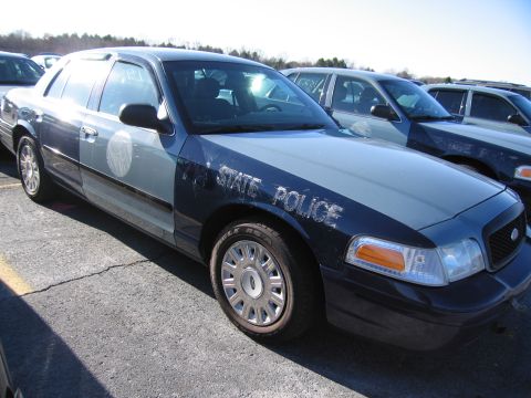 2001 Ford Crown Victoria - A two-tone blue and gray Ford Crown Victoria police car is parked in a lot with other vehicles visible.