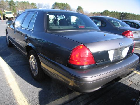 2001 Ford Crown Victoria - A dark sedan with a Ford emblem on the trunk is parked outdoors with other vehicles nearby.