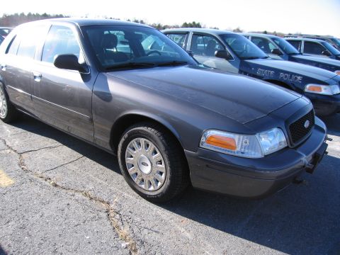 2001 Ford Crown Victoria - A row of dark-colored police vehicles, including a Ford Crown Victoria, are parked in an outdoor lot.