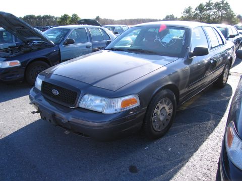 2001 Ford Crown Victoria - A dark gray 2001 Ford Crown Victoria is parked in a lot with its hood open on another vehicle nearby.
