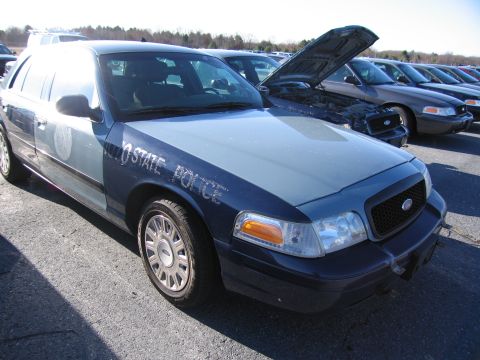 2001 Ford Crown Victoria - A Ford Crown Victoria police car with its hood open is parked in a lot with other vehicles.