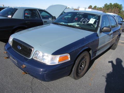 2001 Ford Crown Victoria - A two-tone Ford Crown Victoria is parked in a lot with another similar vehicle behind it.