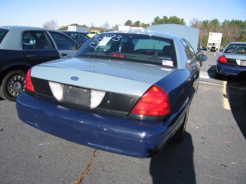 2001 Ford Crown Victoria - A two-tone blue and gray Ford Crown Victoria is parked in a lot with its hood open, alongside other vehicles.