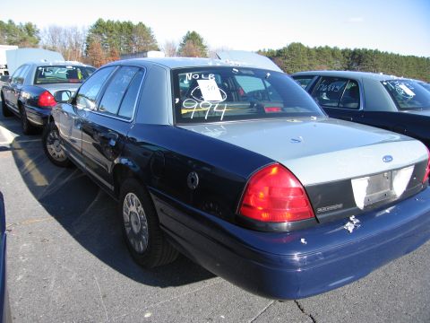 2001 Ford Crown Victoria - A dark blue and silver Ford Crown Victoria is parked in a lot with other vehicles. Numbers are visible on the rear window.