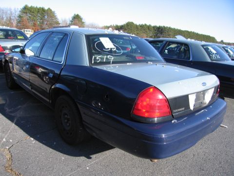 2001 Ford Crown Victoria - A dark blue and grey 2001 Ford Crown Victoria is parked in a lot with other vehicles, showing markings on its rear window.