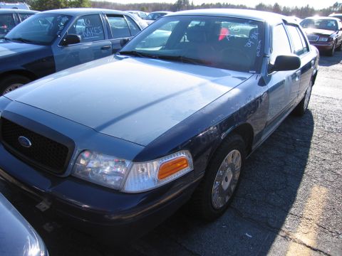 2001 Ford Crown Victoria - A blue and black 2001 Ford Crown Victoria is parked in a lot with other vehicles, showing text on the windshield.