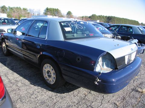 2001 Ford Crown Victoria - A dark blue and silver sedan is parked in a lot with other vehicles, showing damage to the rear.