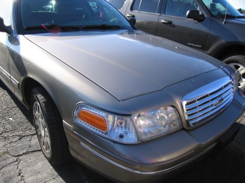 2001 Ford Crown Victoria - The front end of a gray Ford Crown Victoria is visible, with a chrome grille and headlights.