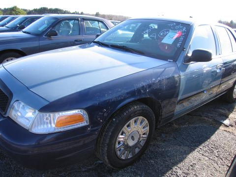 2001 Ford Crown Victoria - A two-tone blue 2001 Ford Crown Victoria is parked in a lot with other vehicles, showing signs of wear and tear.