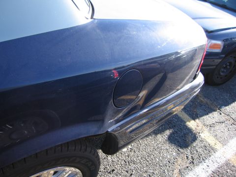 2001 Ford Crown Victoria - The rear quarter panel of a dark blue sedan shows significant damage near the fuel door. Another vehicle is parked nearby.
