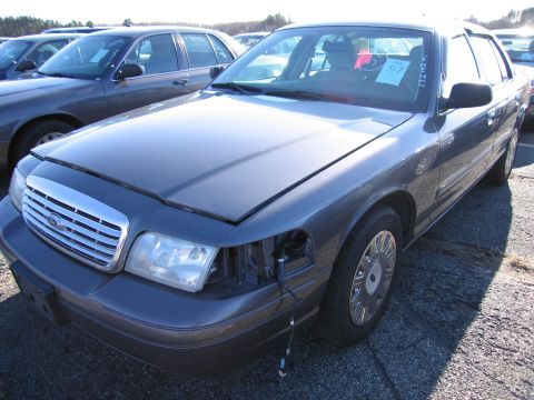 2001 Ford Crown Victoria - A dark gray 2001 Ford Crown Victoria is parked in a lot with its hood open and one headlight missing.