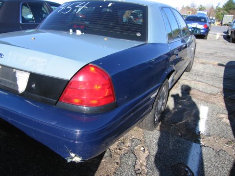 2001 Ford Crown Victoria - The rear of a 2001 Ford Crown Victoria shows damage to the bumper and a number written on the window.