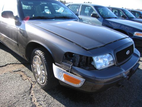 2001 Ford Crown Victoria - A row of Ford Crown Victorias are parked outside, one with damage to its front end.