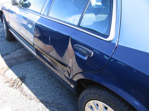 2001 Ford Crown Victoria - A dent is visible on the rear passenger door of this blue sedan.