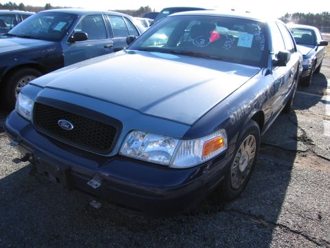 2001 Ford Crown Victoria - A blue 2001 Ford Crown Victoria is parked in a lot with other vehicles. VIN tags are visible on the windshield.
