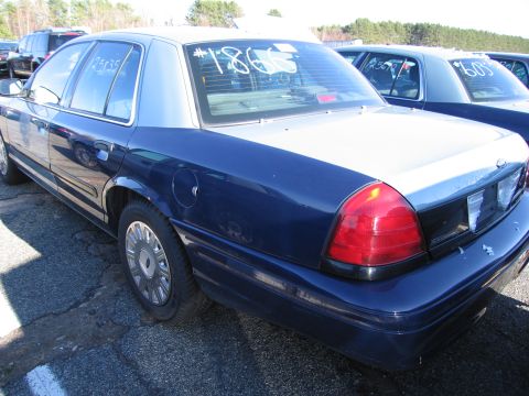 2001 Ford Crown Victoria - A blue and silver Ford Crown Victoria is parked outdoors with other vehicles, showing writing on its windows.