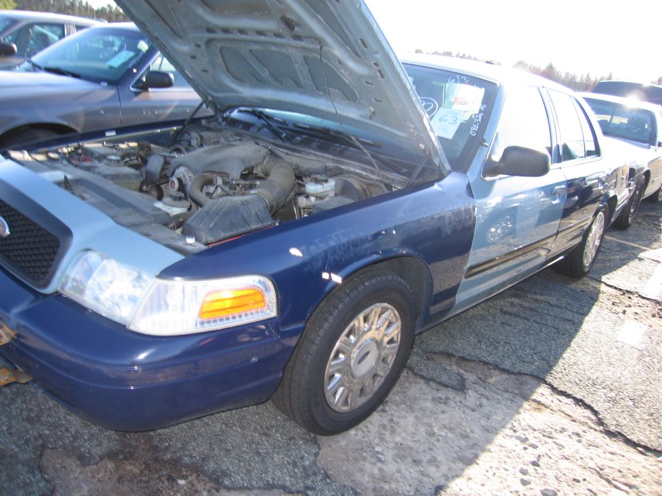 Blue and light blue 2001 Ford Crown Victoria with hood open, parked on cracked asphalt
