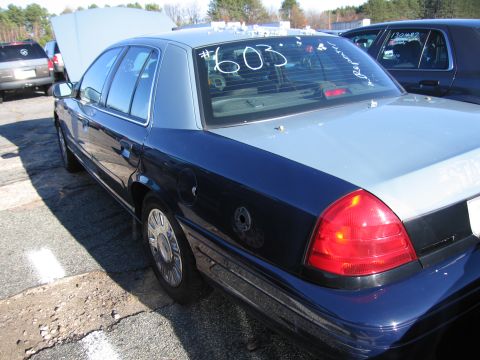2001 Ford Crown Victoria - A two-tone police car, likely a 2001 Ford Crown Victoria, is seen in a lot with other vehicles.