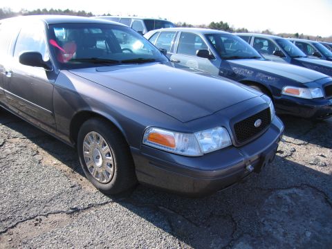 2001 Ford Crown Victoria - A row of dark sedans, including a 2001 Ford Crown Victoria, are parked outdoors on a sunny day.