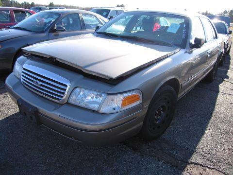2001 Ford Crown Victoria - A tan Ford Crown Victoria sits in a lot with its hood open, parked next to other vehicles.
