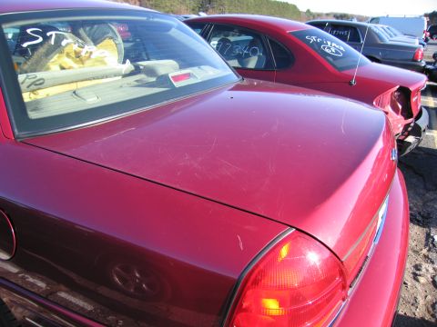 2001 Ford Crown Victoria - Rear view of a red sedan with visible scratches on the trunk and text on the rear window.