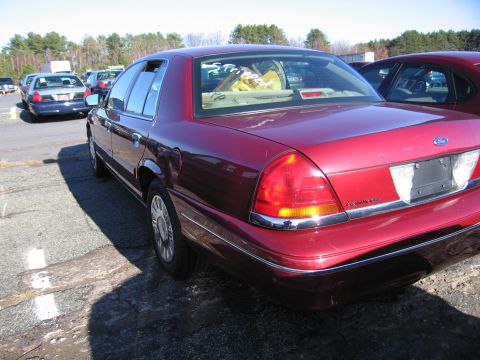 2001 Ford Crown Victoria - Rear view of a red 2001 Ford Crown Victoria, showing its taillights and chrome trim. Other vehicles are visible in the background.