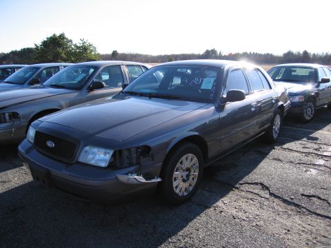 2001 Ford Crown Victoria - A row of Ford Crown Victorias are parked outside under a clear sky, with one in the foreground showing damage to its front end.