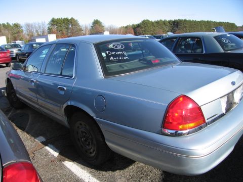 2001 Ford Crown Victoria - A light blue 2001 Ford Crown Victoria is parked in an outdoor lot, with "Devens Auction" visible on the rear window.