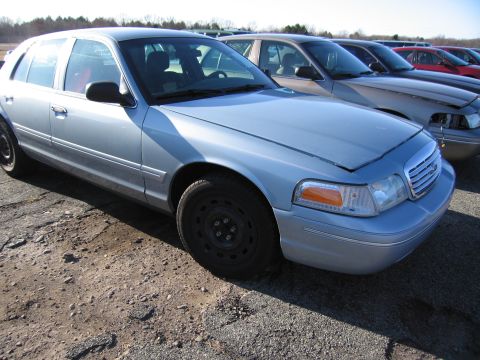 2001 Ford Crown Victoria - A light blue 2001 Ford Crown Victoria is parked in a lot with other vehicles visible in the background.