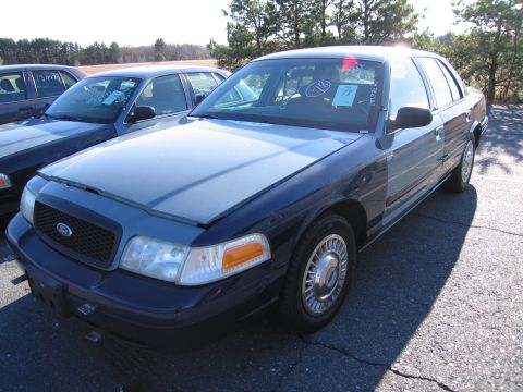2001 Ford Crown Victoria - Two Ford Crown Victorias are parked in an outdoor lot under a bright sky. One car's hood is open.