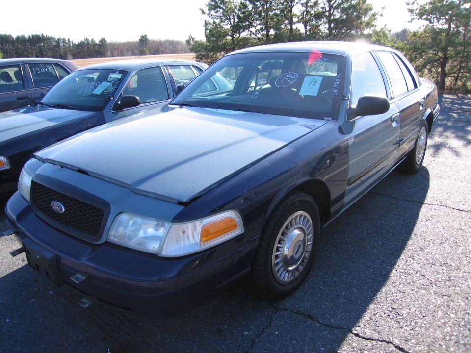 Front view of a dark blue 2001 Ford Crown Victoria parked next to another similar car. The hood is slightly ajar