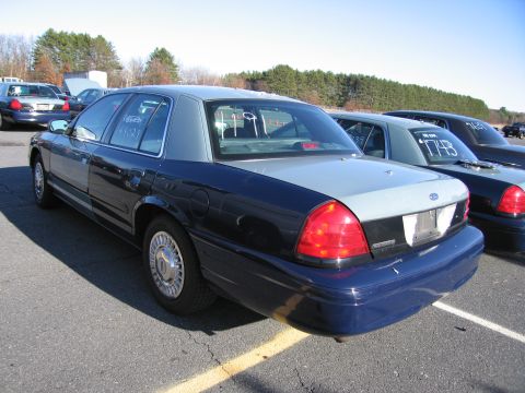 2001 Ford Crown Victoria - A row of sedans, including a 2001 Ford Crown Victoria, are parked outdoors under a clear sky.