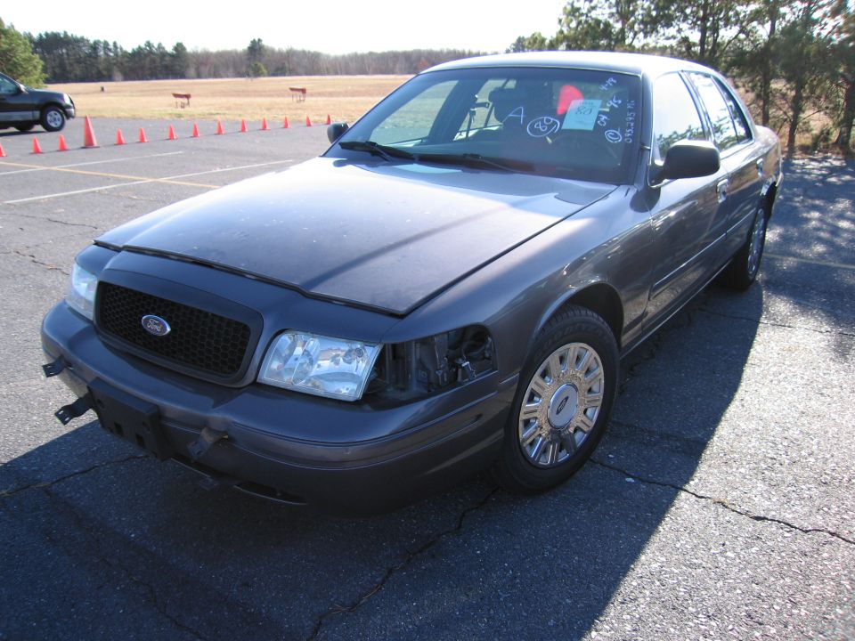 Dark gray 2001 Ford Crown Victoria with missing headlight, hood open, parked on asphalt
