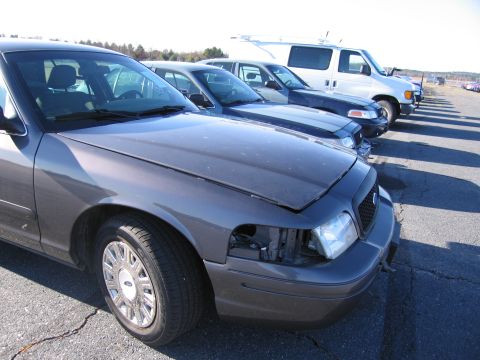 2001 Ford Crown Victoria - A gray 2001 Ford Crown Victoria is parked in a lot, showing damage to its front passenger side headlight assembly.