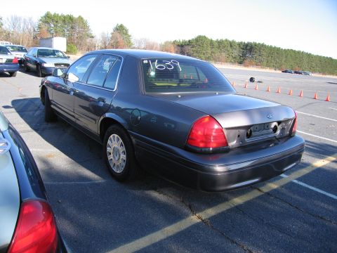 2001 Ford Crown Victoria - A dark sedan is parked in an outdoor lot with orange cones in the background. The number 1639 is visible on the rear window.