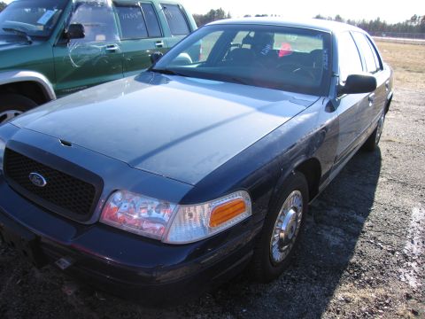 2001 Ford Crown Victoria - A dark blue and gray 2001 Ford Crown Victoria is parked next to a green SUV on a gravel lot.