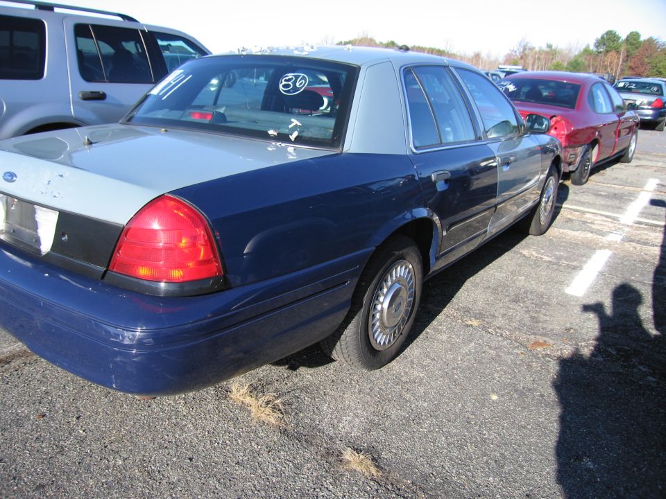 Rear quarter view of a blue and gray 2001 Ford Crown Victoria parked next to a silver SUV and a red car