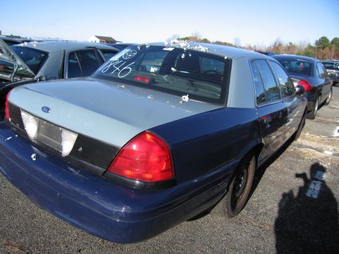 2001 Ford Crown Victoria - A 2001 Ford Crown Victoria is parked in a lot with other vehicles under a clear sky.
