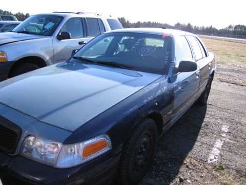 2001 Ford Crown Victoria - Two vehicles parked outdoors, one is a blue and grey Ford Crown Victoria.